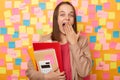 Amazed excited surprised woman wearing beige jacket, holding paper folder, being at work, sees something surprised, covering mouth Royalty Free Stock Photo