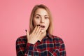 Amazed female with opened mouth, covers it with hand, being shocked to watch something awful on television, dressed in fashionable Royalty Free Stock Photo
