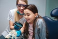 Amazed girl sit in dental chair in room. She look at artificial jaw with teeth. Female dentis hold loop and sit beside Royalty Free Stock Photo