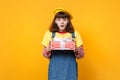 Amazed girl teenager in french beret, denim sundress holding red striped present box with gift ribbon isolated on yellow Royalty Free Stock Photo