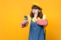 Amazed girl teenager in french beret, denim sundress holding, using mobile phone, put hand on face isolated on yellow Royalty Free Stock Photo