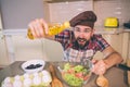 Amazed and happy guy stands at table in kitchen and holds bottle of oil. He poures some of it into bowl with salad. Guy Royalty Free Stock Photo