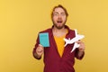 Amazed hipster tourist guy in beanie hat, checkered shirt holding paper plane and passport, shocked