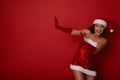 Amazed Hispanic woman dressed in Santa`s clothes holds a copy space on a red background and leans away from it. Conceptual studio