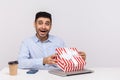 Amazed joyful man employee sitting in office workplace, opening gift box and looking at camera surprised