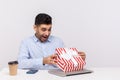 Amazed man sitting in office workplace, opening gift box and looking inside with surprised joyful expression