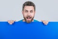 amazed mature bearded man behind blank blue paper banner with copy space for advertising, marketing