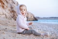 Amazed,open eyed caucasian baby girl sitting on beach eating anf playing with sand by blue sea.Happy,pretty,adorable Royalty Free Stock Photo