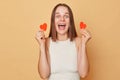 Amazed overjoyed brown haired young woman wearing casual clothing standing isolated over beige background showing little red Royalty Free Stock Photo