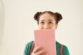 Amazed pretty young woman covered her face with pink book