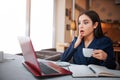 Amazed and scared yougn woman look at laptop screen. She hold one hand on cheek. Another has cup of coffee.