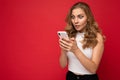 Amazed shocked beautiful young blonde woman wearing white t-shirt  over red background using smartphone and Royalty Free Stock Photo