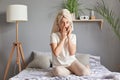 Amazed shocked woman sitting on bed talking on the phone wearing white towel on head gossiping covering mouth with hand looking at Royalty Free Stock Photo