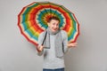 Amazed smirked man in gray sweater, scarf pointing hand, hold colorful umbrella on grey background. Healthy Royalty Free Stock Photo