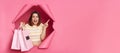 Amazed surprised caucasian young woman wearing striped shirt breaking through pink paper hole holding shopping bags pointing away Royalty Free Stock Photo