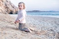 Amazed, surprised sweet little caucasian blonde baby girl with blond curly hair on sandy beach by blue sea.Happy,pretty Royalty Free Stock Photo