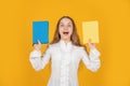 amazed teen girl presenting school workbook on yellow background, education