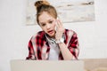 Amazed teenager in checkered shirt and headphones talking on smartphone.