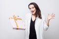 Amazed woman with big surprised eyes and open mouth in white coat standing and holding present with yellow bow showing open Royalty Free Stock Photo