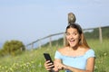 Amazed woman using phone finding wild bird on her head