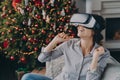 Amazed woman wearing virtual reality glasses first time, sitting on sofa at home near Christmas tree Royalty Free Stock Photo