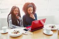 Amazed young african woman sit at table. They look amazed on laptop. Food and drink are on table.