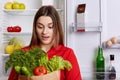 Amazed young female with surprised expression looks at vegetables, forgets to buy something in grocer`s shop, stands in kitchen ne