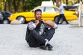 Amazed young man seated down on pavement road with crossed legs, isolated on a yellow blurred taxi background