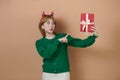 Amazed young Santa girl in fun decorative deer horns on head pointing index finger on red boxes with gifts presents Royalty Free Stock Photo