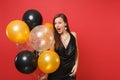 Amazed young woman in little black dress celebrating holding air balloons isolated on red background. St. Valentine`s Royalty Free Stock Photo