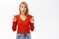 Amazed young woman looks surprised, cross fingers for good luck, standing over white background