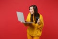 Amazed young woman in yellow fur sweater holding credit bank card, laptop pc computer isolated on bright red wall Royalty Free Stock Photo