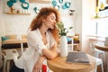 Amazing beautiful redhead young lady posing in cafe smells flowers. Royalty Free Stock Photo