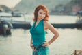 Amazing beautifull lady girl woman with red flame hair wearing fancy fashion green clothes posing sitting on wooden pier jetty wth