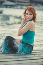 Amazing beautifull lady girl woman with red flame hair wearing fancy fashion green clothes posing sitting on wooden pier jetty wth