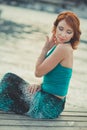 Amazing beautifull lady girl woman with red flame hair wearing fancy fashion green clothes posing sitting on wooden pier jetty wth