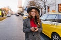 Amazing businesswoman in tweed coat walking down the road near yellow taxi. Glad long-haired woman in hat posing on the Royalty Free Stock Photo