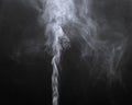 Amazing closeup abstract view of vertical, smooth stream of white grayish smoke on dark background
