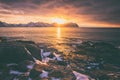 Amazing colors of north atlantic sunset, winter seascape with ocean, rocky seacoast, beautiful cloudy sky, snowy mountains and sun