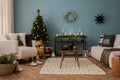 Amazing and cozy christmas living room interior with modular sofa, boucle armchair, wooden consola, candlestick, christmas tree,
