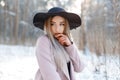 Amazing glamorous pretty beautiful young woman in a luxurious black hat in a stylish pink warm coat posing on a sunny day