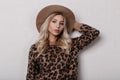 Amazing glamorous young blond woman in a fashionable beige hat in a stylish leopard sweater with curly hair