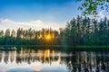 Amazing landscape with northern lake and forest on summer evening at sunset. Sunbeams among pine trees, reflection in water. Royalty Free Stock Photo