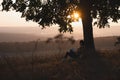 Amazing landscape, young girl with book sitting under big tree, colorful forest and sunset on the background Royalty Free Stock Photo