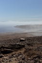 Amazing lonely lake shore in early morning with soft haze above smooth tranquil water with pebble coast and cape in fog. Liveless.