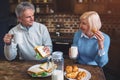 Amazing and old people are eating meal at the table in kitchen.