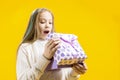 Amazing reaction. The girl looks delightedly at the gift box on a yellow background. Christmas presents Royalty Free Stock Photo