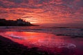 Amazing red colorful sunset at the beach with cloudy sky. Dramatic seascape with clouds and waves. Little town houses in Royalty Free Stock Photo