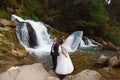 Amazing romantic view of happy bride with groom near beautiful grand waterfall in mountain. luxurious wedding dress. Marriage coup