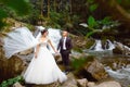 Amazing romantic view of happy bride with groom near beautiful grand waterfall in mountain. luxurious wedding dress. Marriage coup Royalty Free Stock Photo